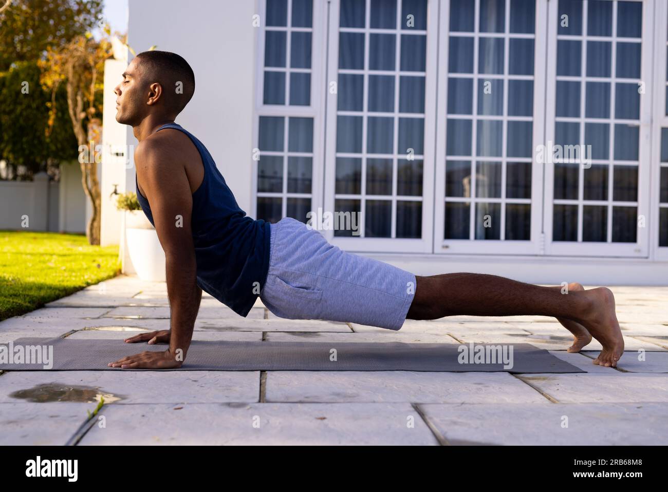 Fokussierter birassistischer Mann, der Yoga im sonnigen Garten praktiziert. Cobra Pose, Sommer, Wohlbefinden, Fitness und gesunder Lebensstil, unverändert. Stockfoto