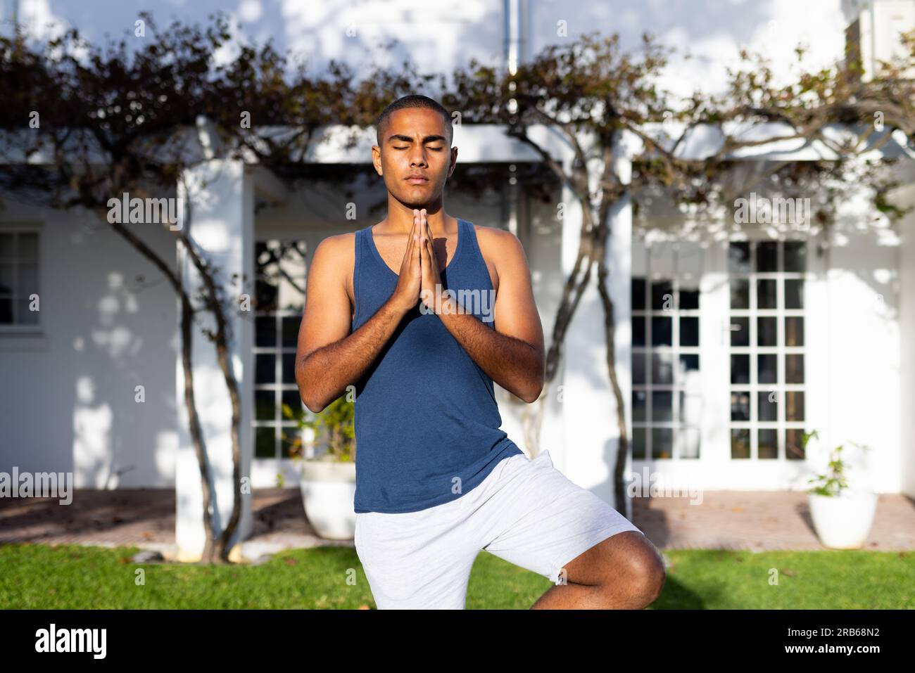 Fokussierter, birassistischer Mann, der Yoga-Meditation praktiziert und im sonnigen Garten steht. Sommer, Wohlbefinden, Fitness und gesunder Lebensstil, unverändert. Stockfoto