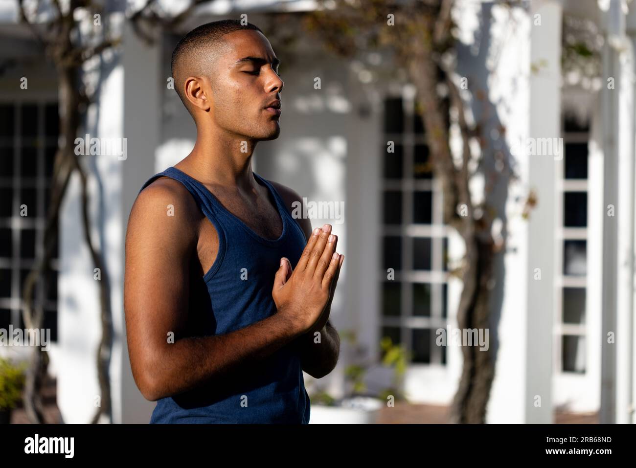 Fokussierter, birassistischer Mann, der Yoga-Meditation praktiziert und im sonnigen Garten steht. Sommer, Wohlbefinden, Fitness und gesunder Lebensstil, unverändert. Stockfoto