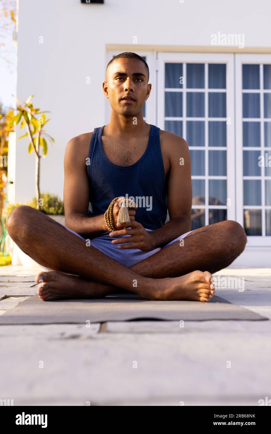 Fokussierter birassistischer Mann, der Yoga-Meditation praktiziert, sitzt im sonnigen Garten, Kopierraum. Sommer, Wohlbefinden und gesunder Lebensstil, unverändert. Stockfoto