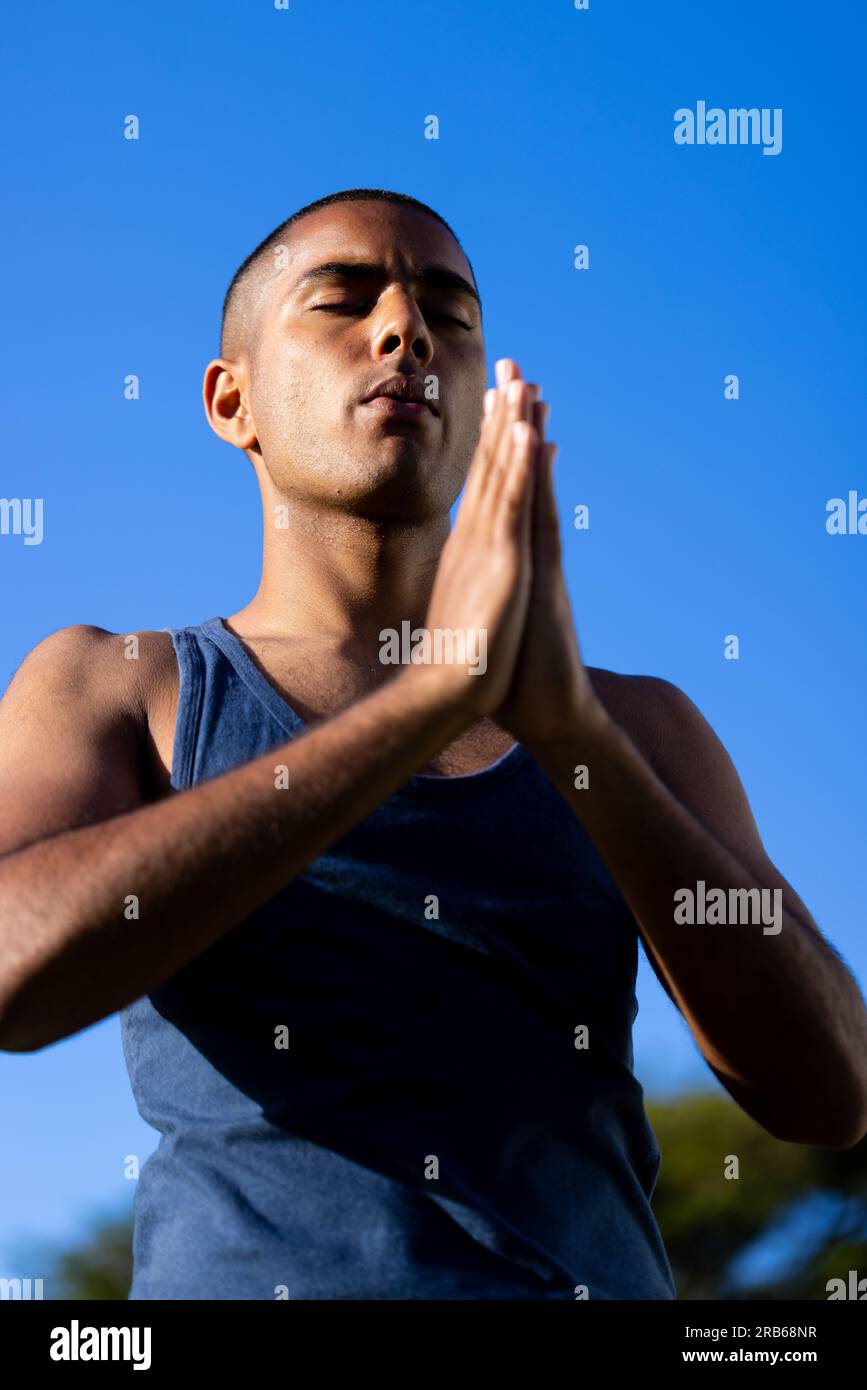 Fokussierter, birassistischer Mann, der Yoga-Meditation in der Sonne vor hellblauem Himmel praktiziert. Sommer, Wohlbefinden, Fitness und gesunder Lebensstil, unverändert. Stockfoto