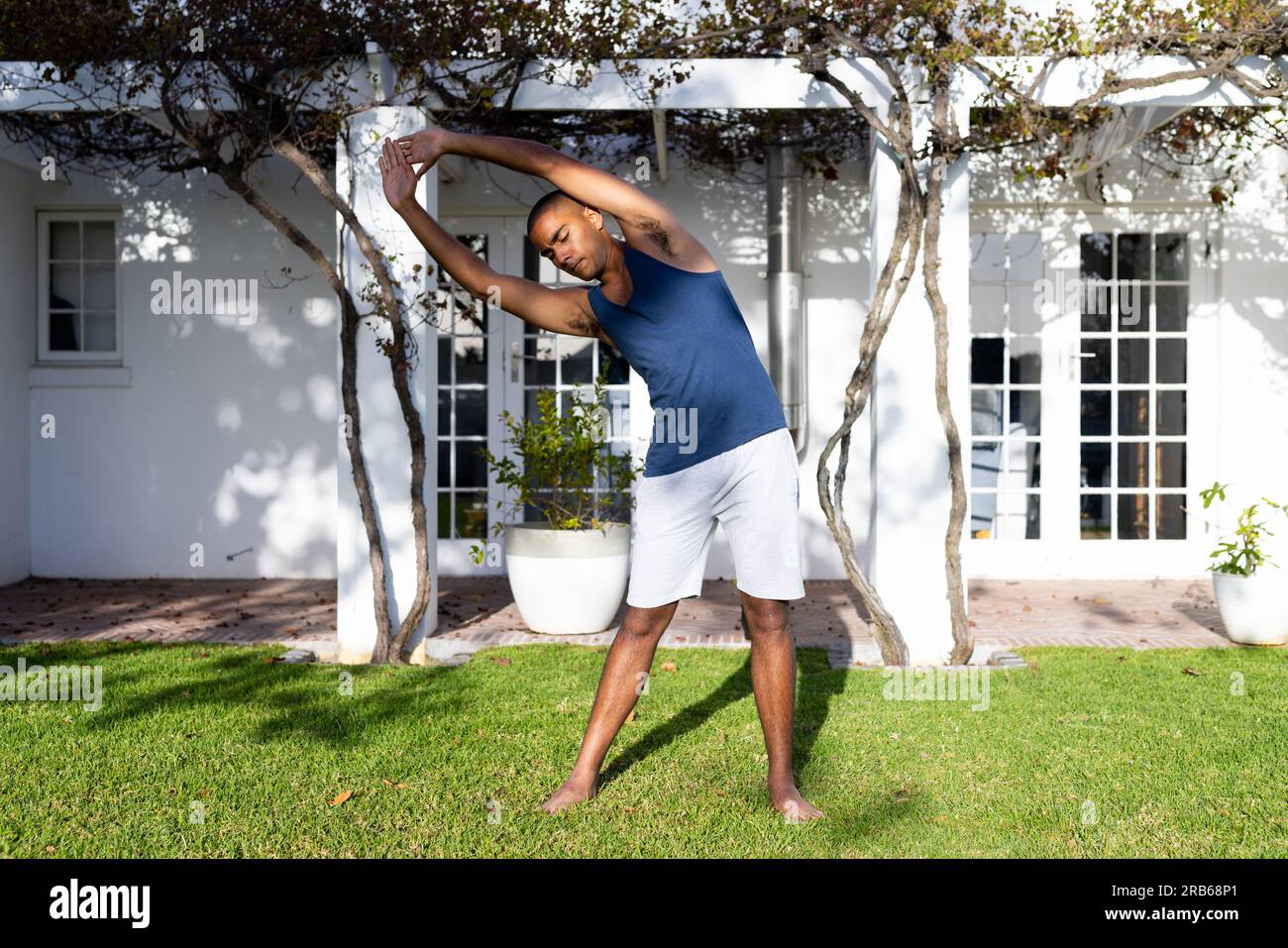 Ein birassischer Mann, der Yoga im sonnigen Garten praktiziert. Sommer, Wohlbefinden, Fitness und gesunder Lebensstil, unverändert. Stockfoto