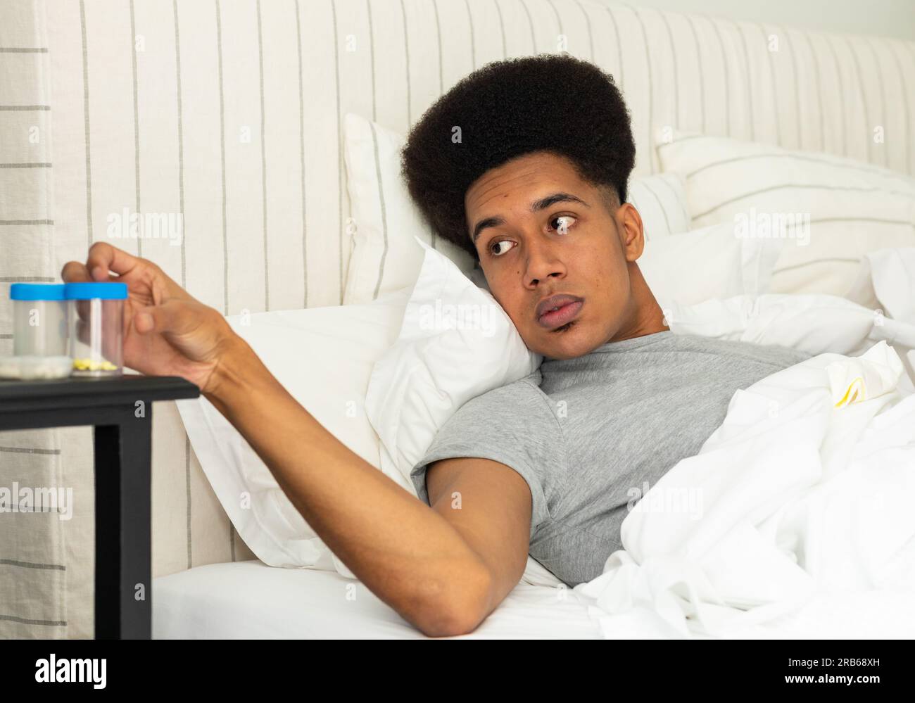 Ein birassischer Mann, der im Bett liegt und nach Medikamenten greift. Medizin, Gesundheitswesen, Wohlbefinden, Lebensstil und häusliches Leben, unverändert. Stockfoto