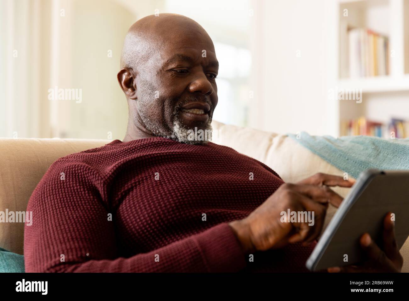 Glücklicher afroamerikanischer Seniorist, der ein Tablet im sonnigen Wohnzimmer benutzt. Seniorenleben, Ruhestand, Kommunikation und häusliches Leben, unverändert. Stockfoto