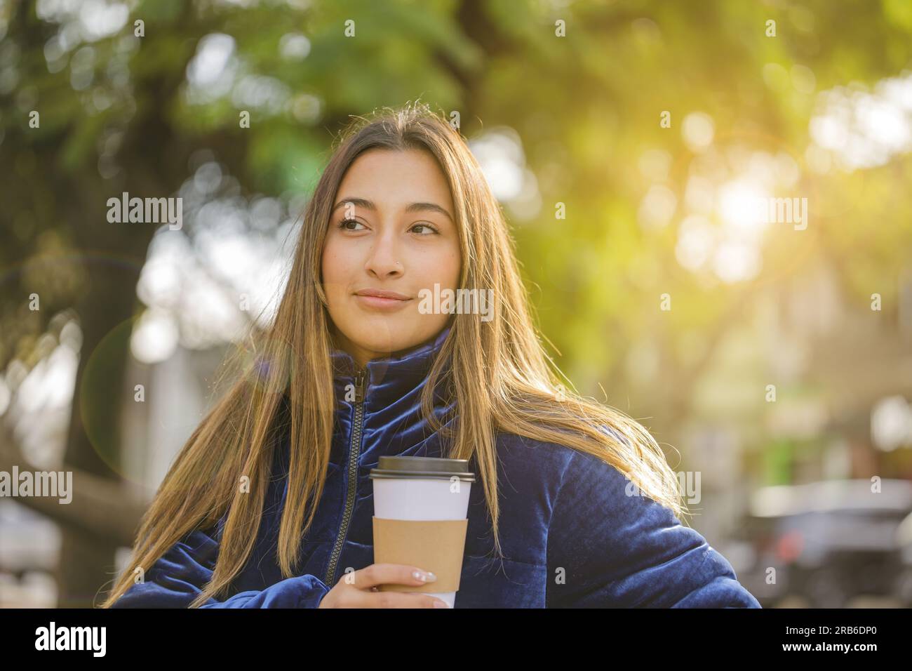 Porträt eines wunderschönen lateinischen Mädchens, das Kaffee trinkt, auf einer öffentlichen Parkbank mit Kopierbereich. Stockfoto