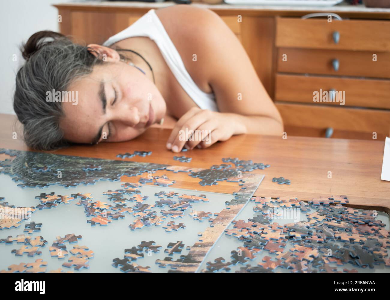 Eine Frau schläft auf einem Holztisch ein, während sie ein Puzzle zusammenstellt. Konzept von Ermüdung, Aufgeben Stockfoto