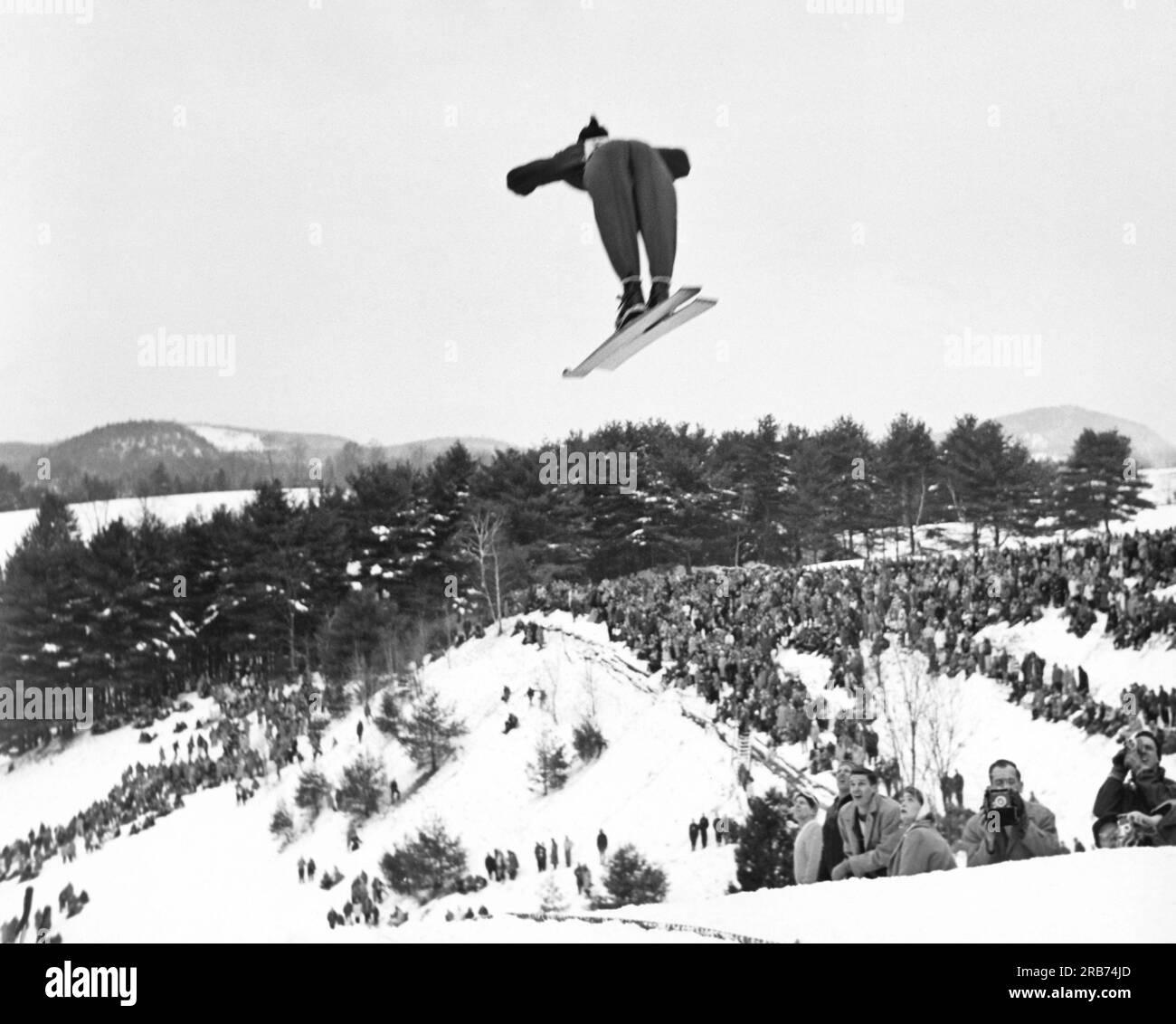 Hannover, New Hampshire: c. 1955 Rückblick auf einen Skifahrer, der beim jährlichen Winterkarneval des Dartmouth Outing Clubs von der Skisprungschanze abspringt. Stockfoto