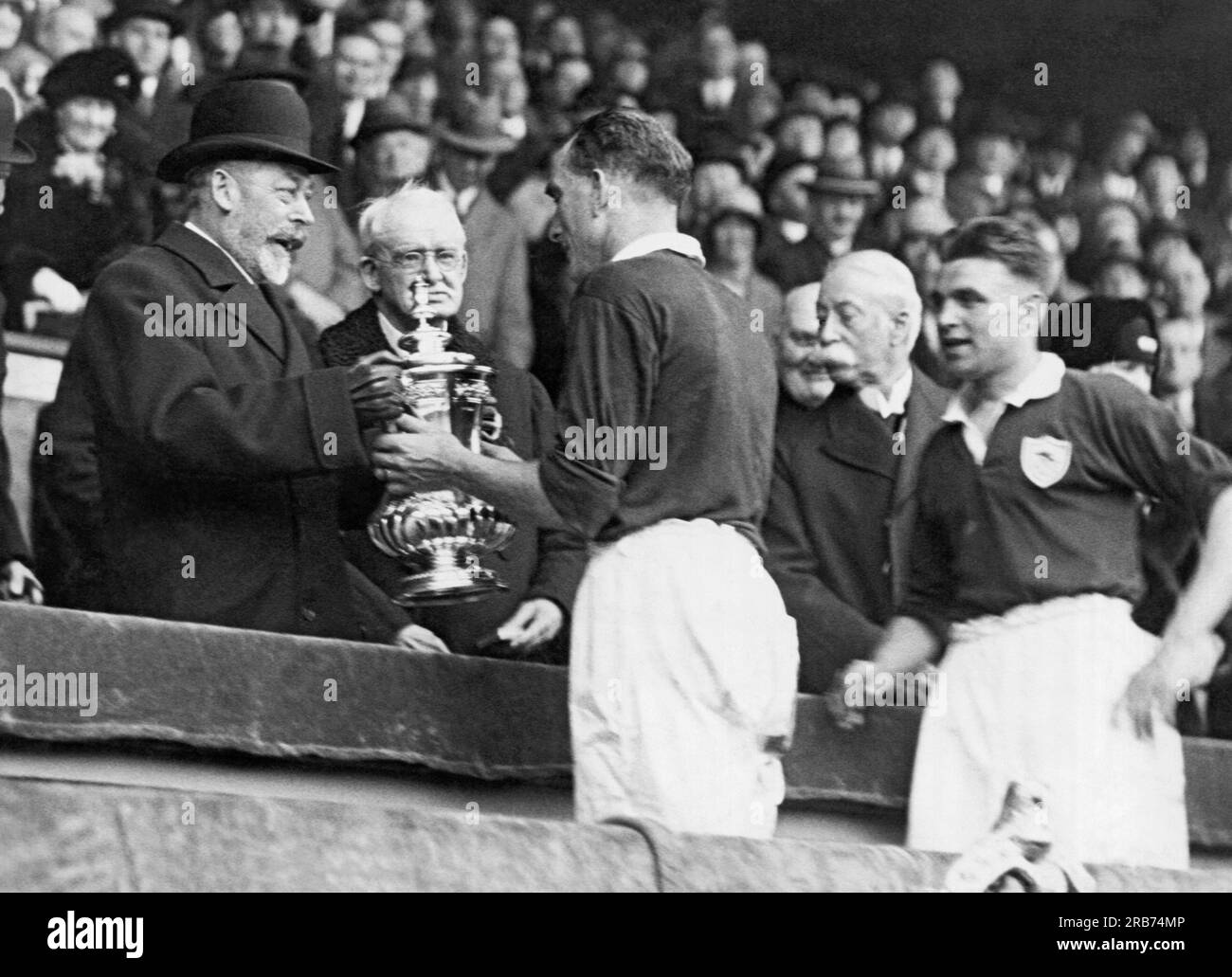 London, England: 1930 King George of England überreicht Mr. Parker, dem Kapitän der Arsenals, die das WM-Finale im Wembley Stadium gewonnen haben, die Trophäe der Fußballvereinigung. Stockfoto