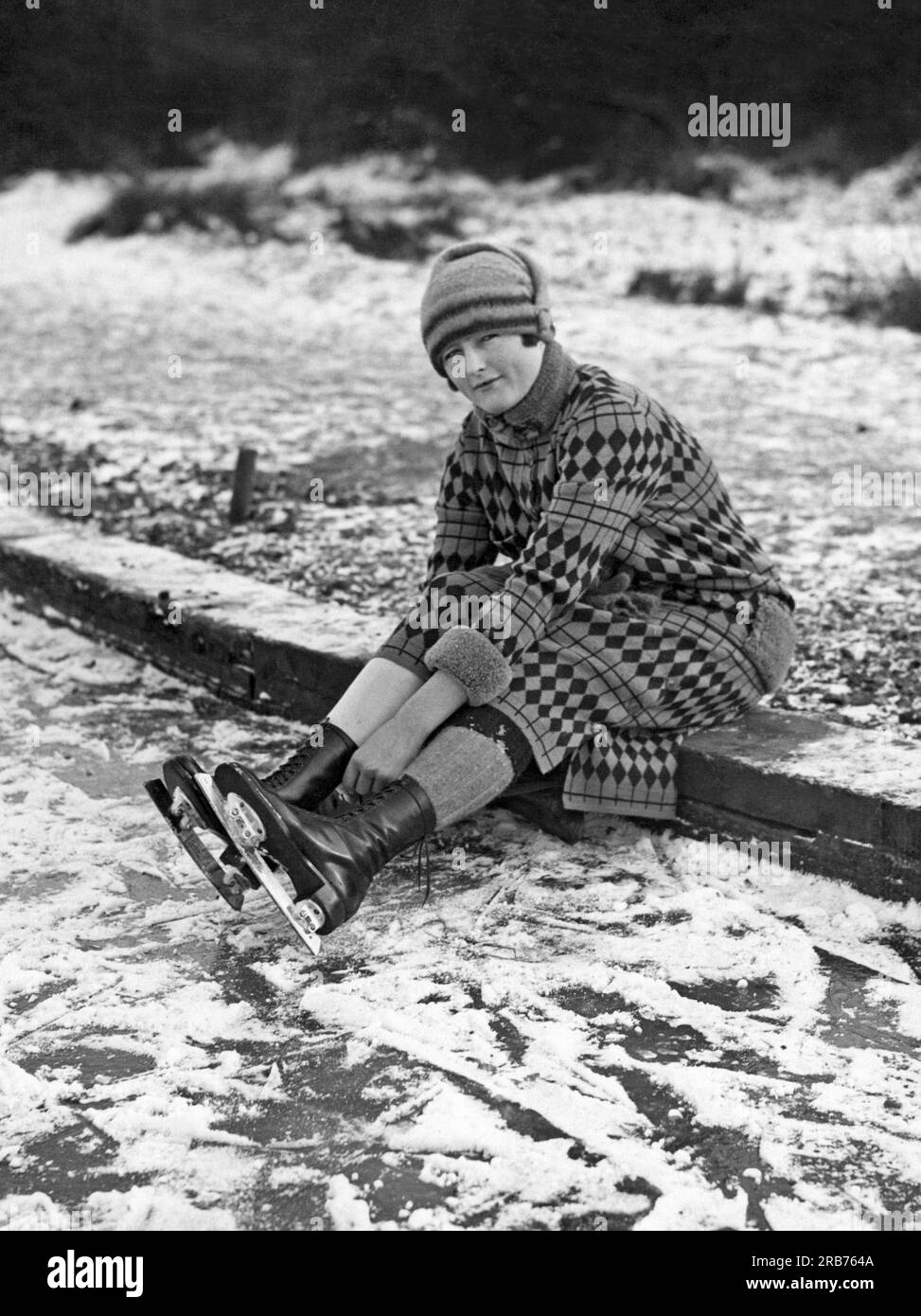 London, England: ca. 1935. Eine Schlittschuhläuferin passt ihre Schlittschuhe auf Connaught Water an, eine Meile östlich von Chingford im Londoner Stadtteil Waltham Forest. Stockfoto