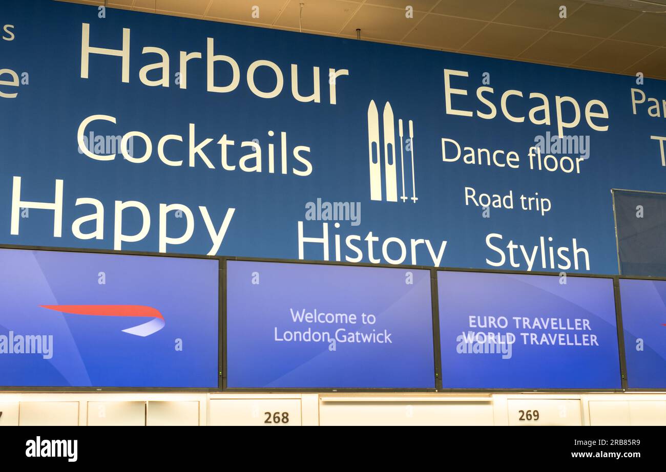 Wörter, die das Reiseerlebnis hinter den Abfertigungsschaltern von British Airways am Flughafen London Gatwick, South Terminal, West Sussex, Großbritannien, fördern. Stockfoto