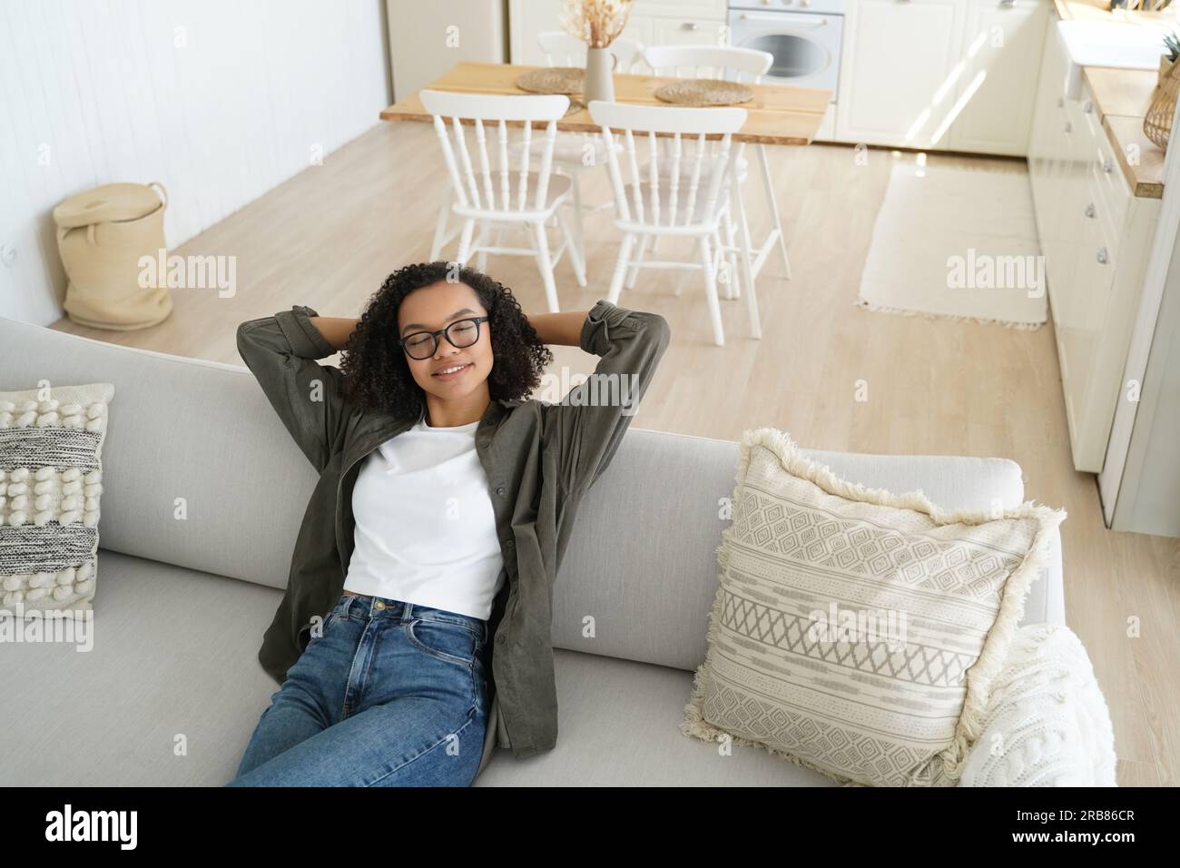 Ein entspanntes Mädchen mit Brille träumt zu Hause auf der gemütlichen Couch. Ruhige Frau genießt faule Pausen, ruht mit den Händen hinter dem Kopf. Stockfoto
