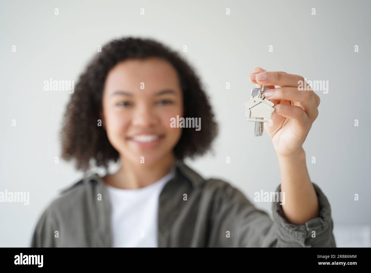 Ein glücklicher, birassistischer Teenager-Hausbesitzer zeigt neue Hausschlüssel. Eine lächelnde Dame hält den Wohnungsschlüssel und konzentriert sich auf die Hand. Hypothekenanzeige. Stockfoto