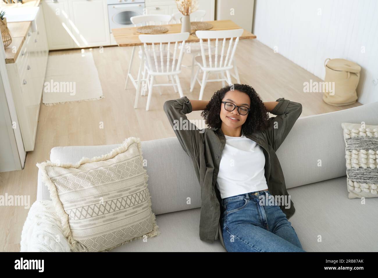Ein entspanntes Mädchen mit Brille träumt zu Hause auf der gemütlichen Couch. Ruhige Frau genießt faule Pausen, ruht mit den Händen hinter dem Kopf. Stockfoto