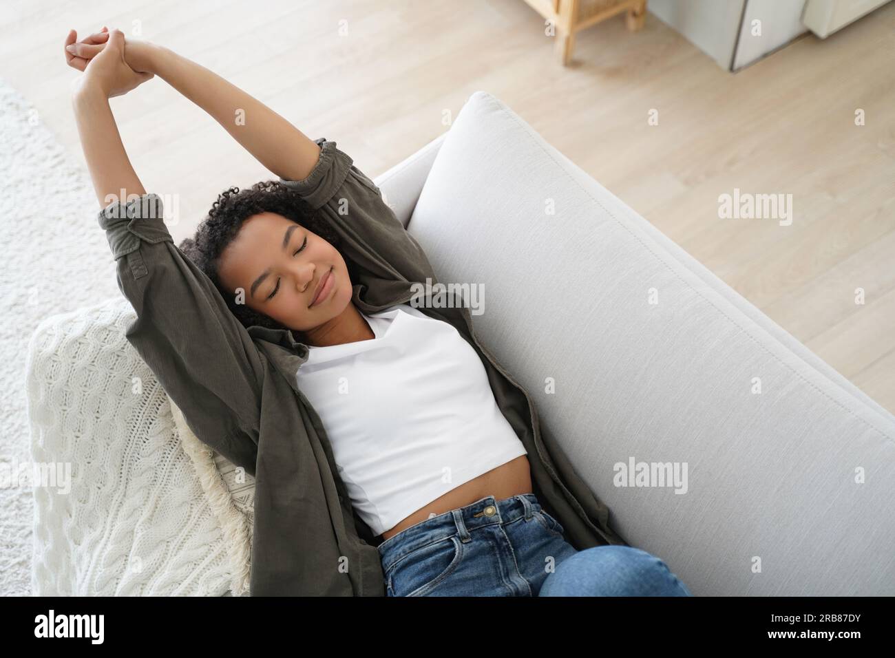 Das entspannte Mädchen dehnt sich zu Hause auf der gemütlichen Couch. Der Teenager wacht nach einem Nickerchen auf, lächelt und genießt ein faules Wochenende. Stockfoto
