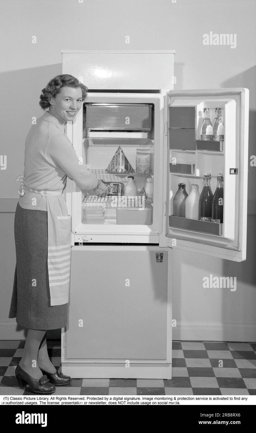 In der Küche 1960er. Eine Frau in ihrer Küche mit offener Tür zum Kühlschrank. Sie können die Lebensmittel verschiedener Arten sehen, die ordentlich in den Regalen ausgestellt sind. Unter anderem ist die klassische Tetran-Milchverpackung sichtbar. Erfunden von Ruben Rausing und der Anfang des Tetra Pak Verpackungsimperiums wurde. Schweden 1960. Conard Ref. 4188 Stockfoto