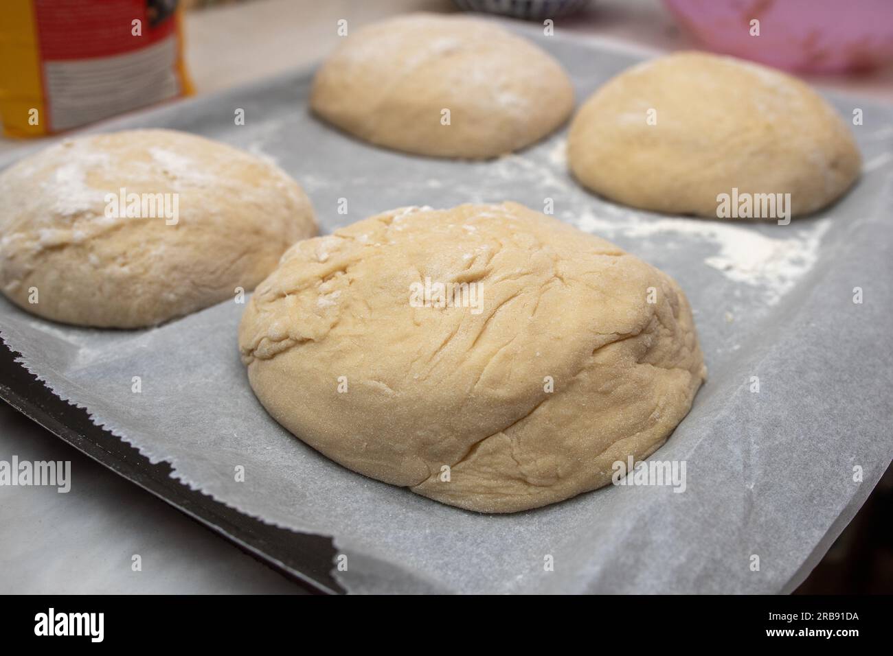 Der Prozess des Backens zu Hause. Nahaufnahme von süßem Brotteig in Form von Brötchen auf einem Tablett, bevor er in den Ofen geht Stockfoto