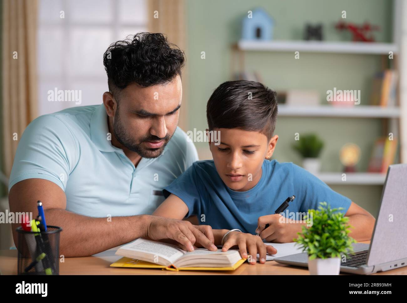 Indischer Vater unterrichtet oder Sohn beim Lesen aus dem Buch zu Hause unterstützt - Konzept der elterlichen Betreuung, Heimunterricht und Tutoring. Stockfoto