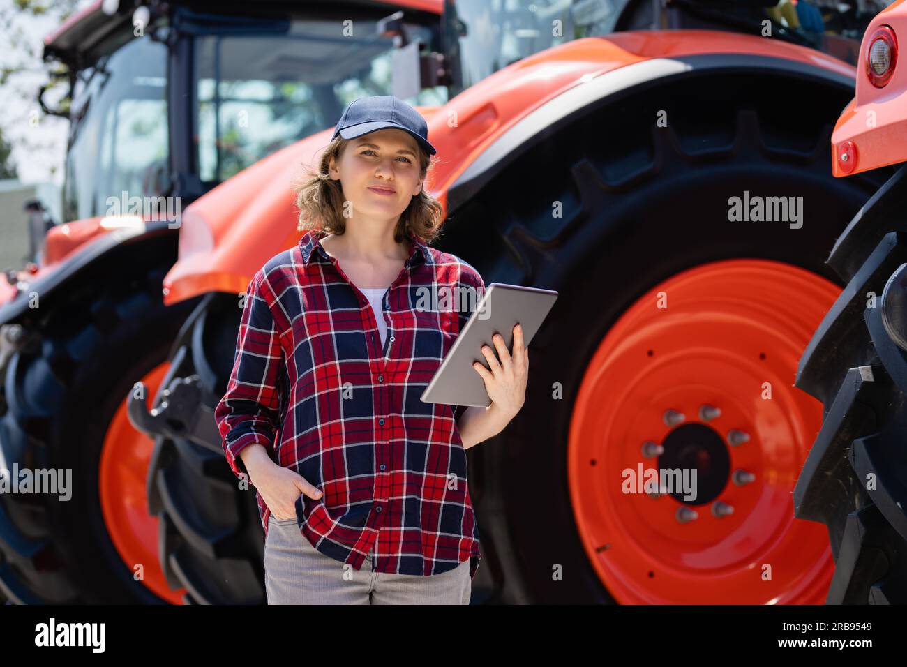 Landwirtin mit einem digitalen Tablet auf dem Hintergrund eines landwirtschaftlichen Traktors Stockfoto