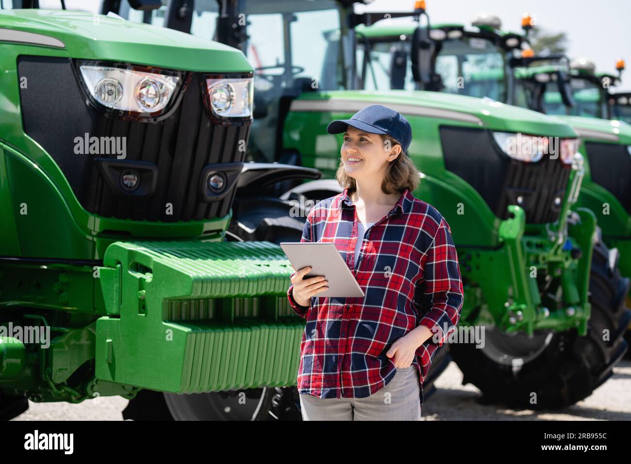 Landwirtin mit einem digitalen Tablet auf dem Hintergrund eines landwirtschaftlichen Traktors Stockfoto