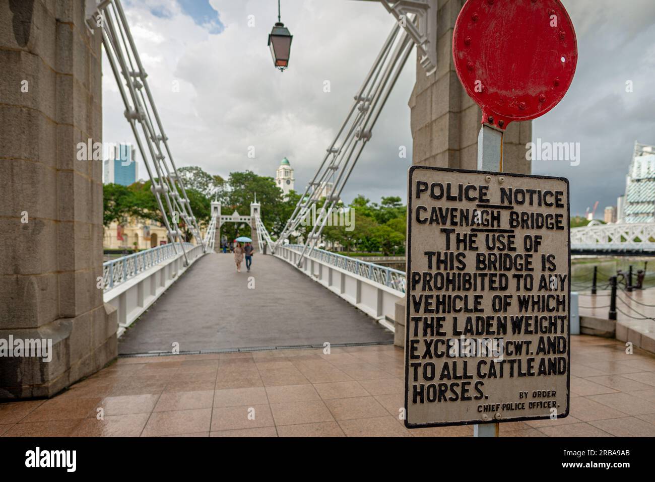 Singapur - 20. Dezember 2022: Altes Modeschild am Eingang der Cavenagh-Brücke. An einem regnerischen Tag mit einem nicht wiedererkennbaren Ehepaar, das mit Verstand läuft Stockfoto