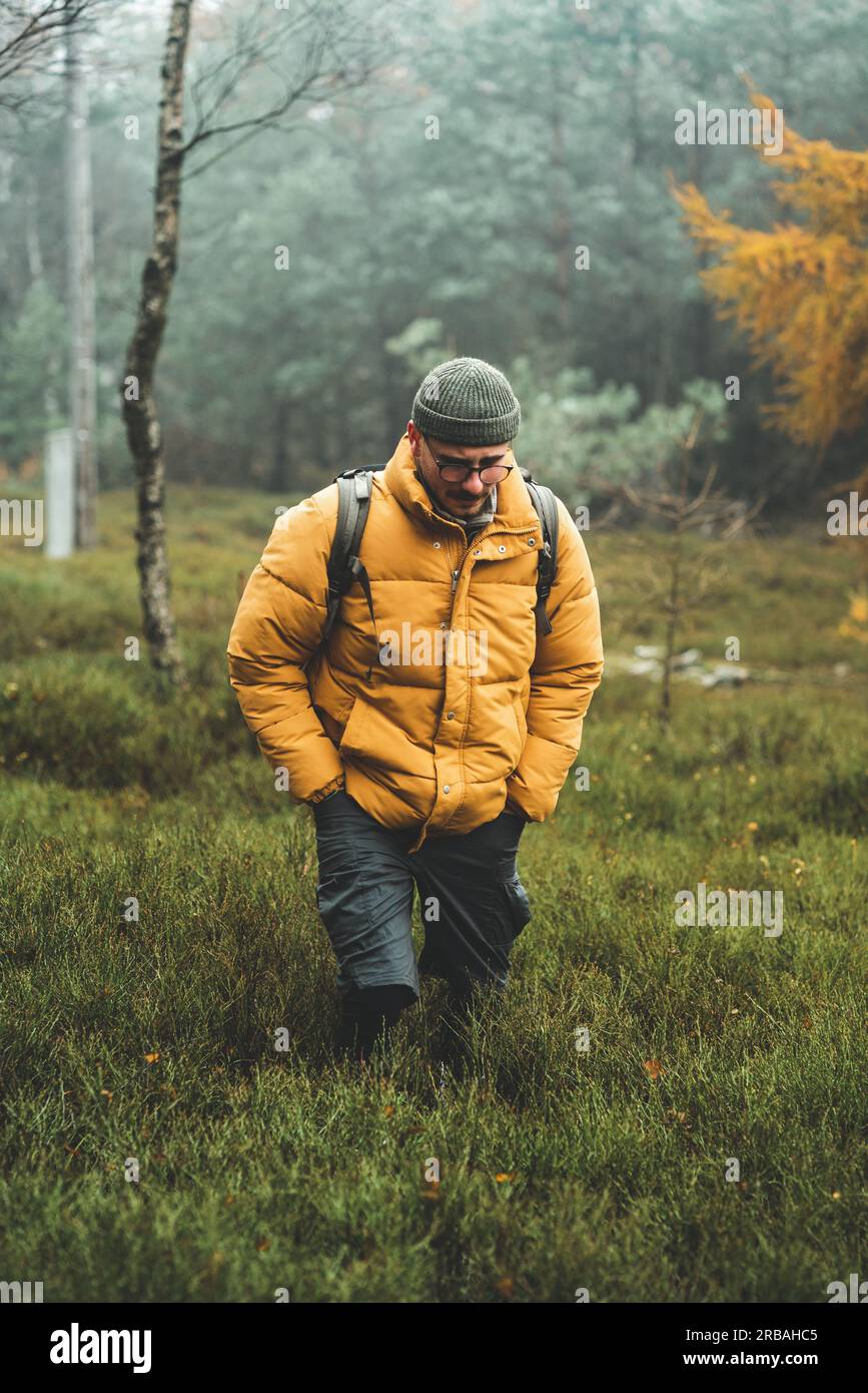 Junger Mann mit gelber Winterjacke und Hut, spaziert durch Birkenwald, während des kalten bewölkten Herbsttags, Decin, Tschechische republik Stockfoto
