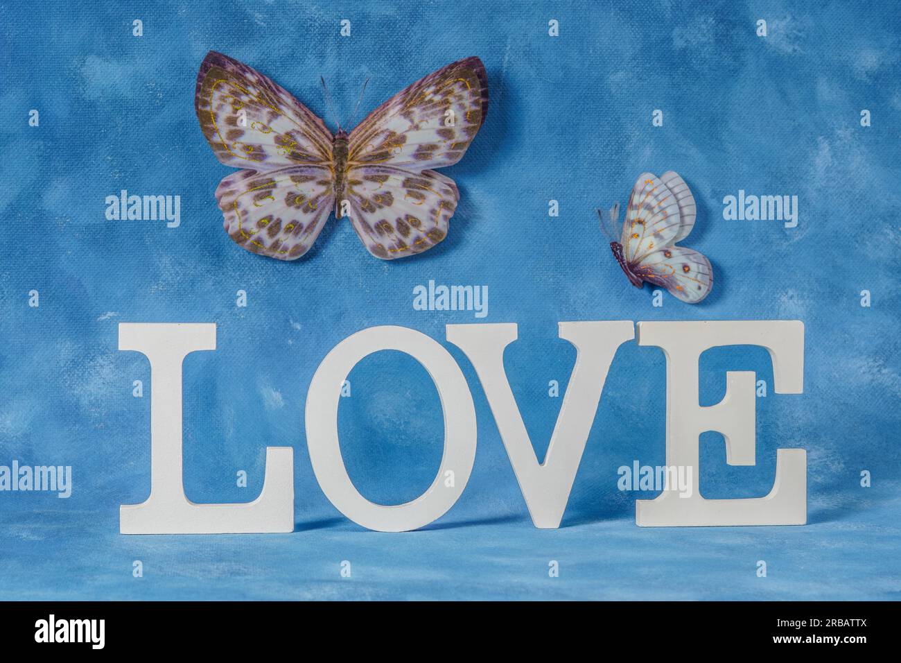 Wort Liebe geschrieben in weißen Holzbriefen mit blauem Hintergrund und fliegenden Schmetterlingen Stockfoto