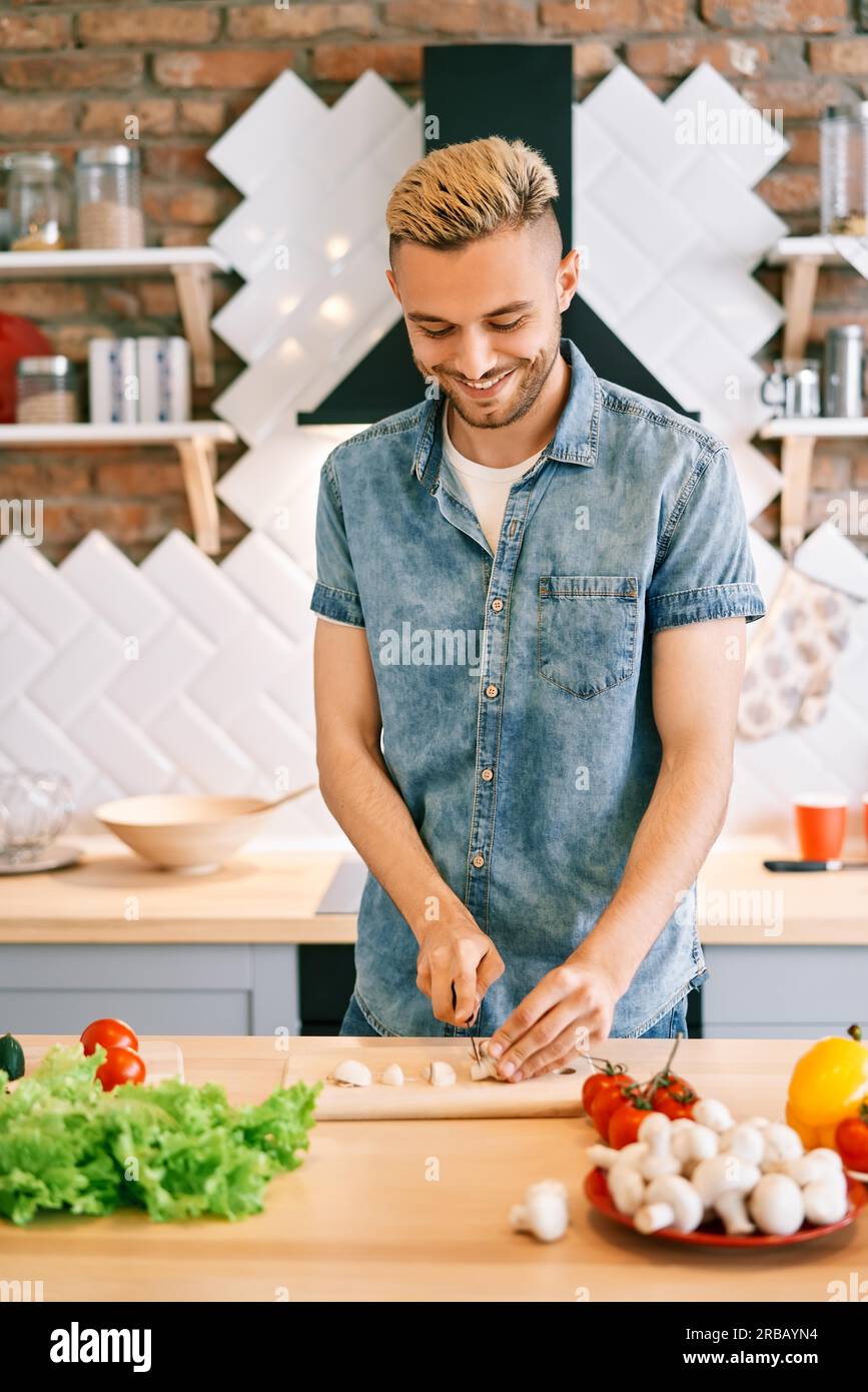 Lächelnder junger Mann, der in der Küche zu Hause gesunde Lebensmittel kocht. Vegane Ernährung Lebensmittelkonzept Stockfoto