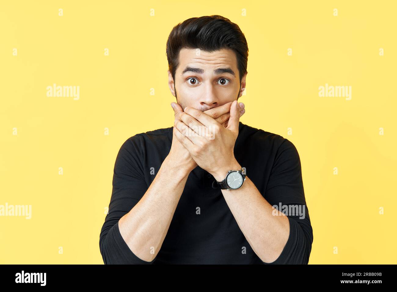 Schockierter Mann, der den Mund mit Händen über gelbem Hintergrund bedeckt. Emotionen und geheimes Konzept Stockfoto