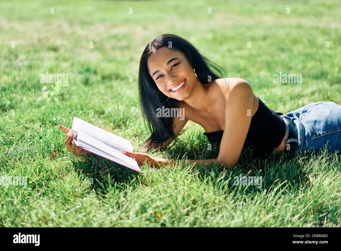 Ziemlich afro amerikanische Frau Buch im Gras im Park liegend zu lesen. Entspannung und Hobby-Konzept Stockfoto