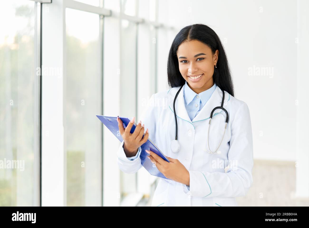 Glücklich lächelnd afroamerikanischen Arzt mit Zwischenablage im Krankenhaus. Medizin, Beruf und Gesundheitskonzept Stockfoto