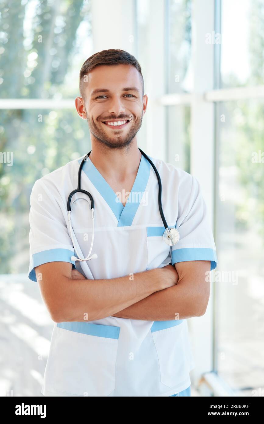 Porträt eines selbstbewussten lächelnden männlichen Arztes mit Stethoskop in medizinischer Uniform, die Arme gekreuzt Stockfoto