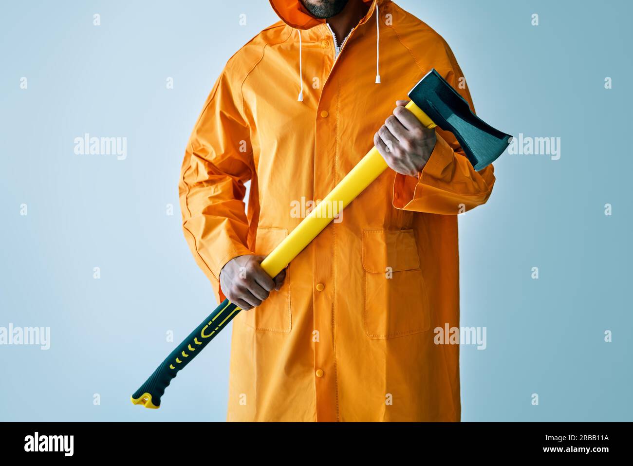 Zugeschnittenes Bild von Mann in hellen Regenmantel hält große Axt. Holzfäller, Fischer mit Axt Stockfoto