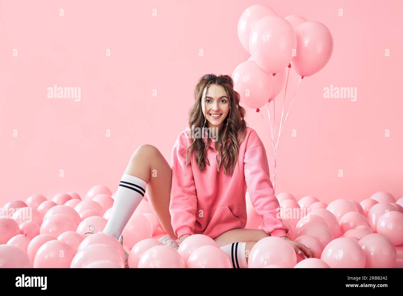 Junge trendige Frau posiert mit rosa Luftballons auf rosa Hintergrund. Pop Art. Feier, festlich, lustiges Konzept Stockfoto