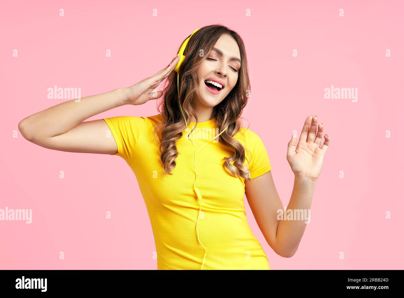 Fröhliche junge Frau, die mit Kopfhörern Musik hört und tanzt Genießen Sie Lieblingslieder auf rosa Hintergrund Stockfoto