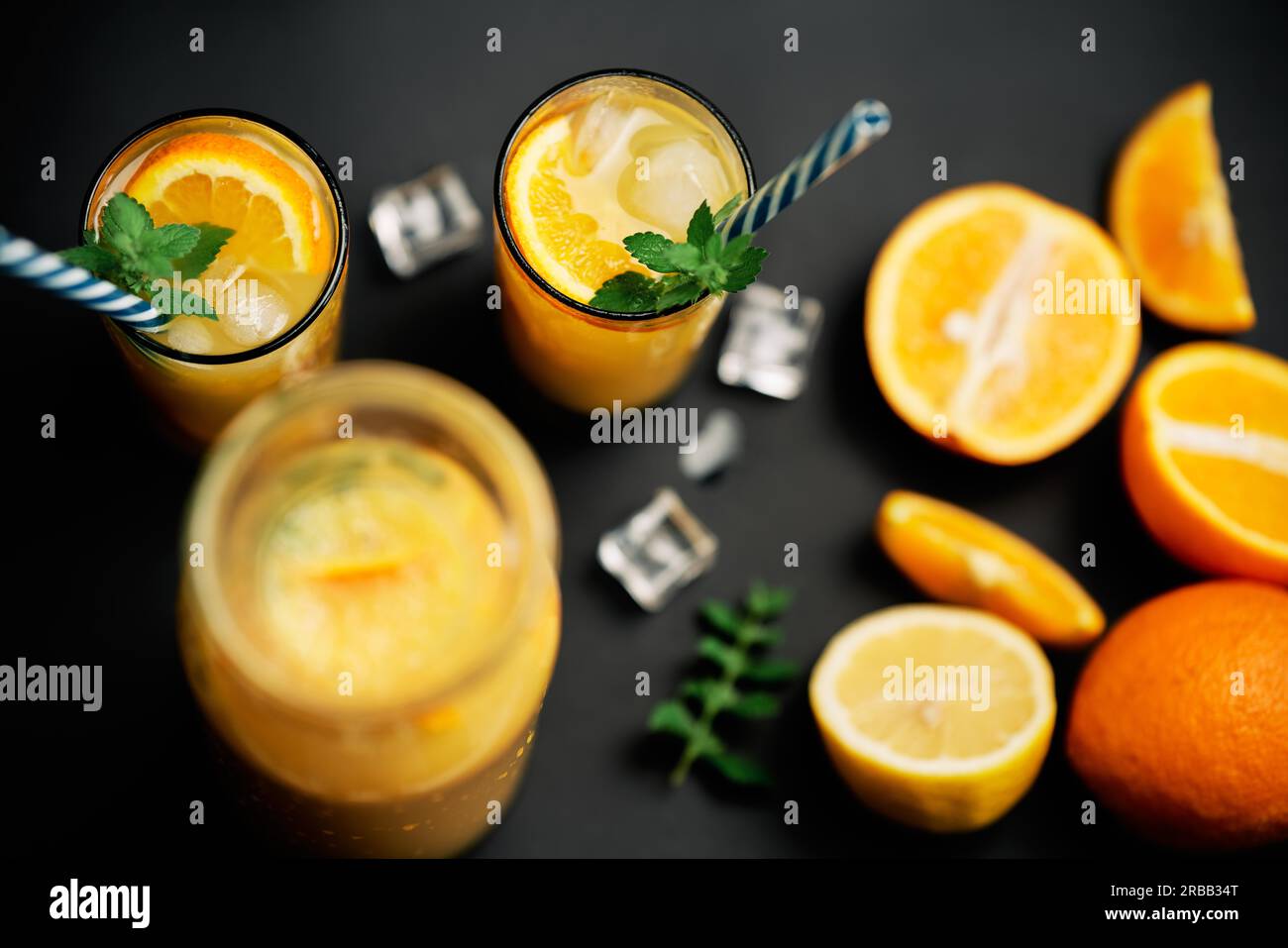 Köstlicher frischer Orangensaft mit Eis, Minze und frischen Früchten auf schwarzem Tischhintergrund. Party, Drink, Gesundheitskonzept Stockfoto