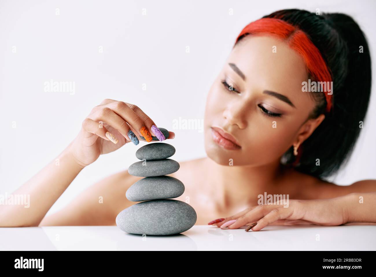Hübsche afroamerikanische Frau, die Pyramide der Steine auf weißem Hintergrund macht. Balance-Konzept Stockfoto