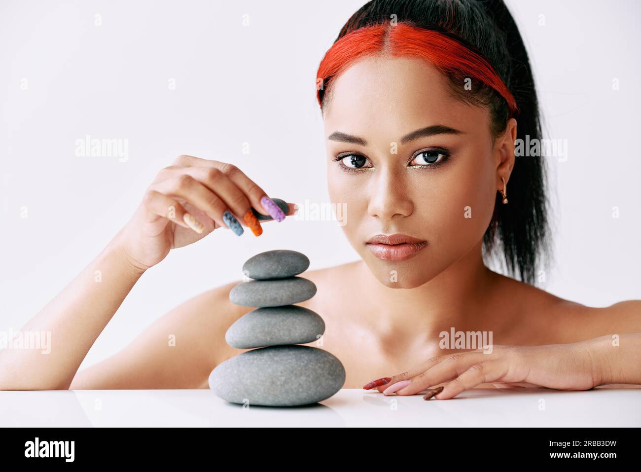 Hübsche afroamerikanische Frau, die Pyramide der Steine auf weißem Hintergrund macht. Balance-Konzept Stockfoto