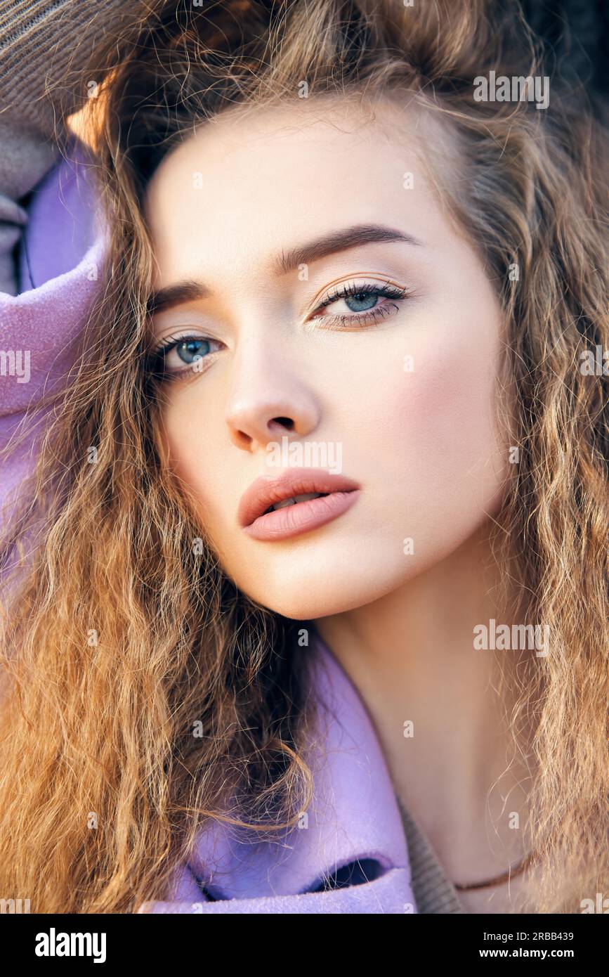 Nahaufnahme eines Porträts einer hübschen jungen Frau mit langen, welligen Haaren bei Sonnenlicht im Freien. Weibliche Schönheit, Make-up und Kosmetik Stockfoto
