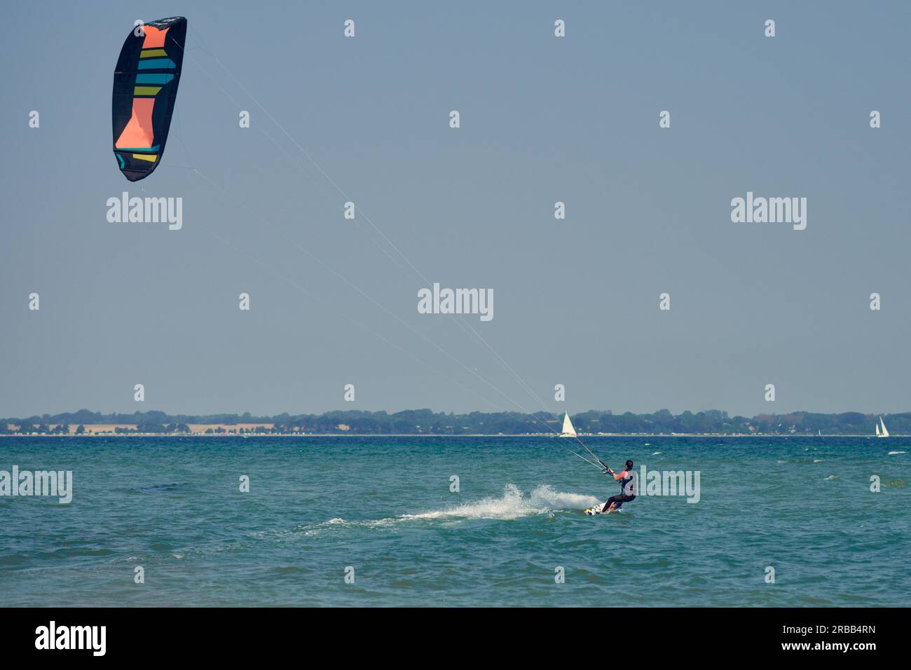 Brünette Frauen beim Kitesurfen oder Drachenboarden, die vom Sandstrand wegfahren, um an einem sonnigen Sommertag tiefes Wasser zu genießen, mit Blick nach hinten Stockfoto