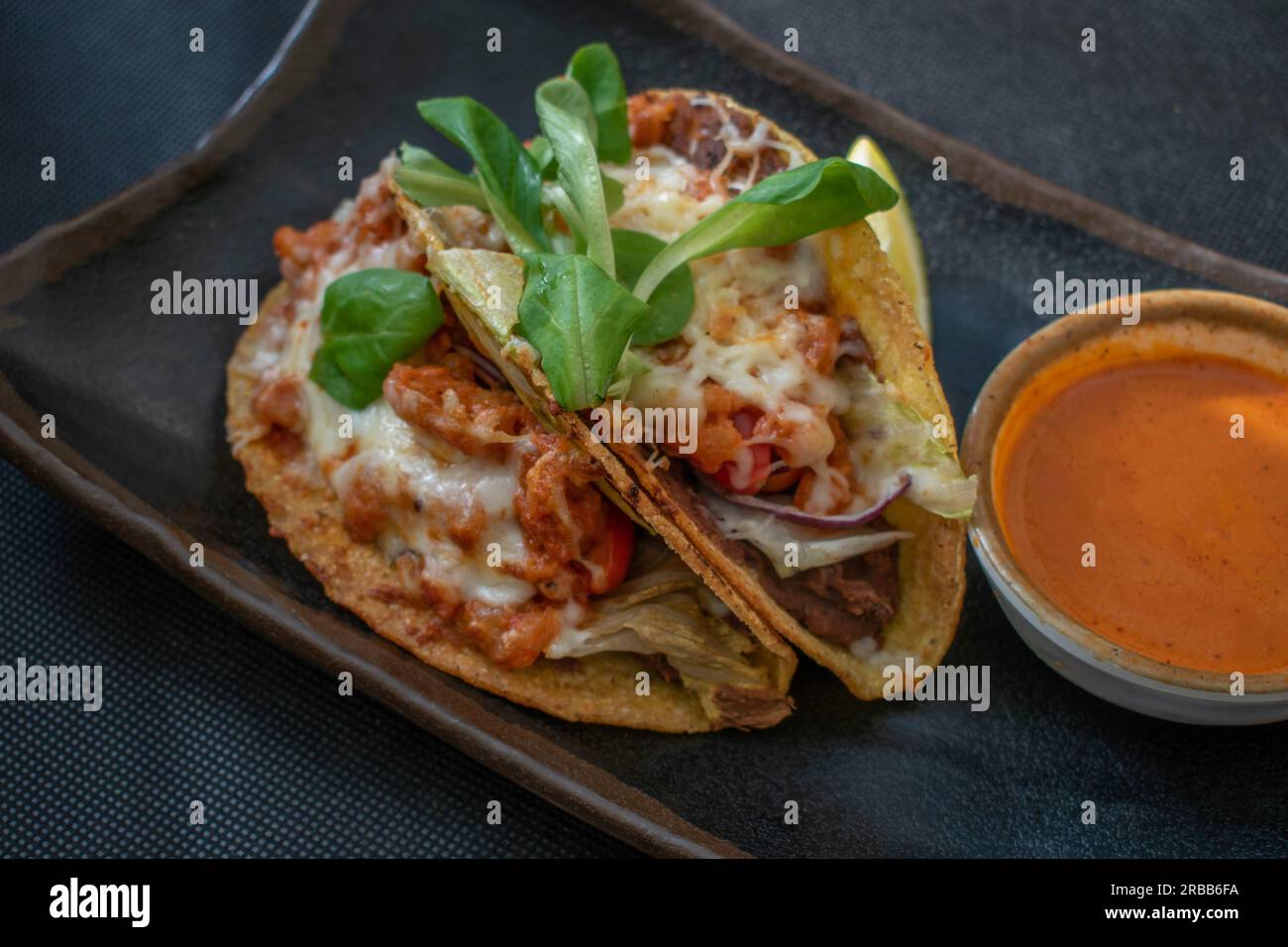 Leckere mexikanische Tacos mit saftigen Garnelen, Tomaten, Käse, Chili und Zwiebeln, Serviert mit einer Beilage heißer und würziger mexikanischer Sauce für einen Stockfoto