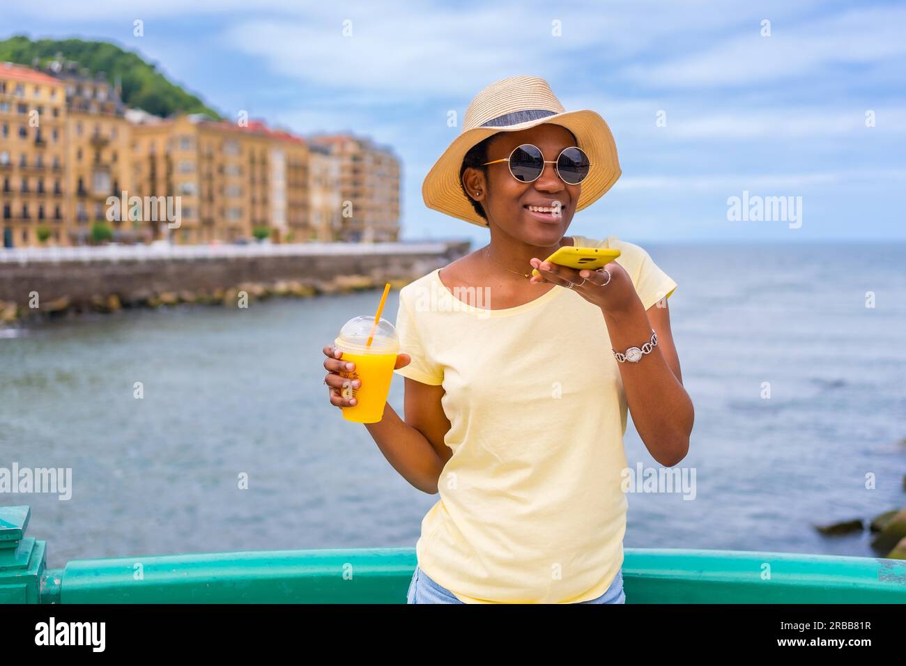 Schwarze ethnische Frau, die Orangensaft am Meer in der Stadt trinkt, Touristen, die den Sommer genießen Stockfoto