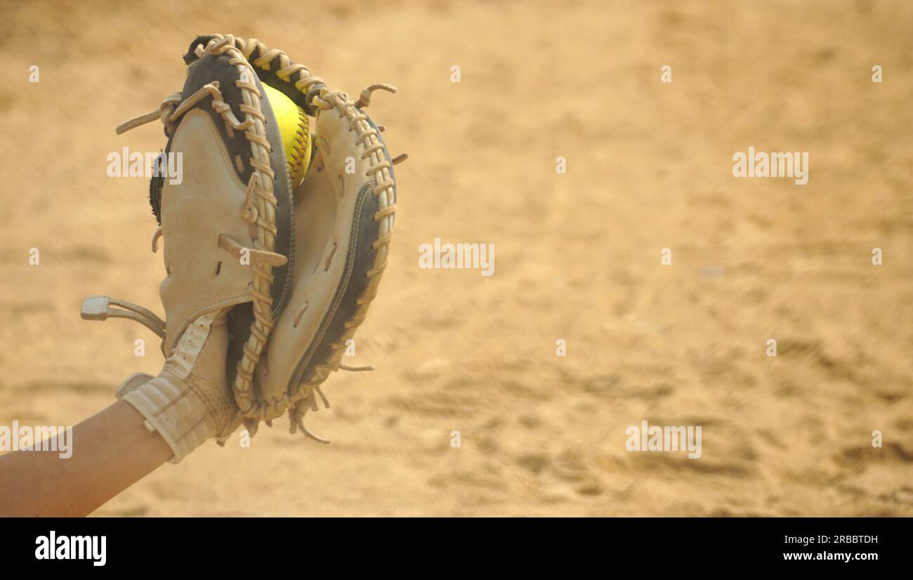 Softball, der in einem Fanghandschuh gefangen ist, mit dem Schmutz des Innenfelds als Kopierraum. Stockfoto
