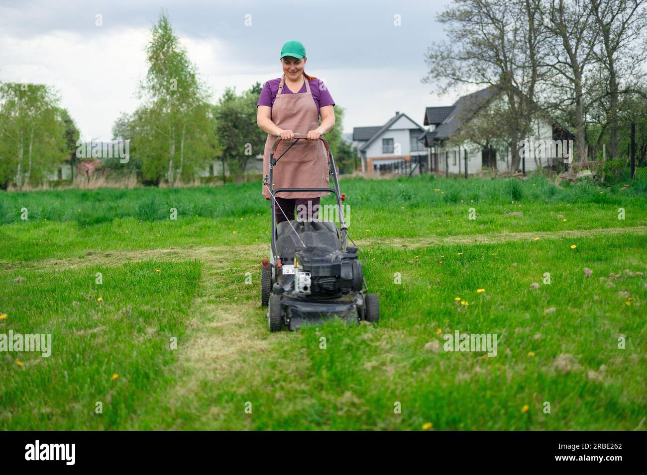 Eine junge Arbeiterin mäht mit einem Rasenmäher in seinem wunderschönen ...