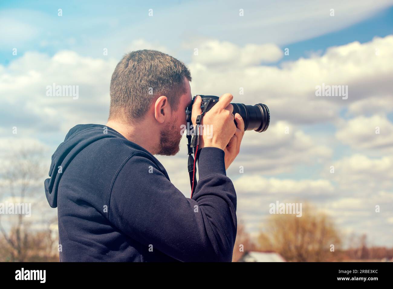 Person, die mit einer Reflexkamera fotografiert. Mann mit schwarzer Fotokamera an warmen Sommertagen Stockfoto