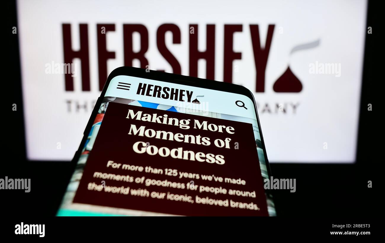 Smartphone mit Webseite des US-amerikanischen Lebensmittelunternehmens The Hershey Company auf dem Bildschirm vor dem Firmenlogo. Fokus auf oberer linker Seite des Telefondisplays. Stockfoto