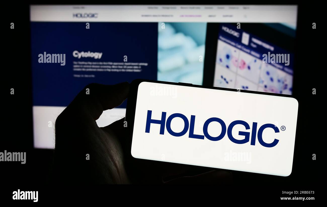 Person, die ein Mobiltelefon mit dem Logo des US-amerikanischen Medizintechnik-Unternehmens Hologic Inc. Auf dem Bildschirm vor der Business-Webseite hält. Konzentrieren Sie sich auf das Display des Telefons. Stockfoto