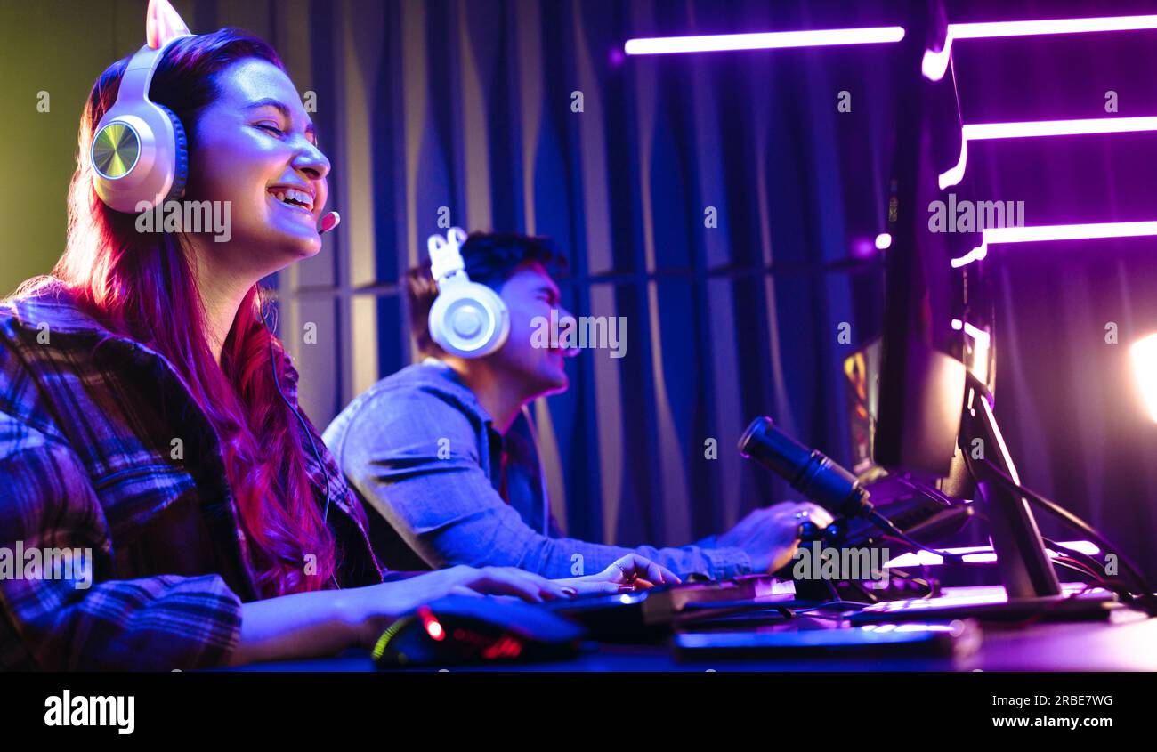 Eine Gamer-Frau, die während eines Wettkampfs glücklich lächelt und ihren Sieg gegen einen männlichen Spieler genießt. Junge Frau dominiert ein Online-Video-Spiel Stockfoto