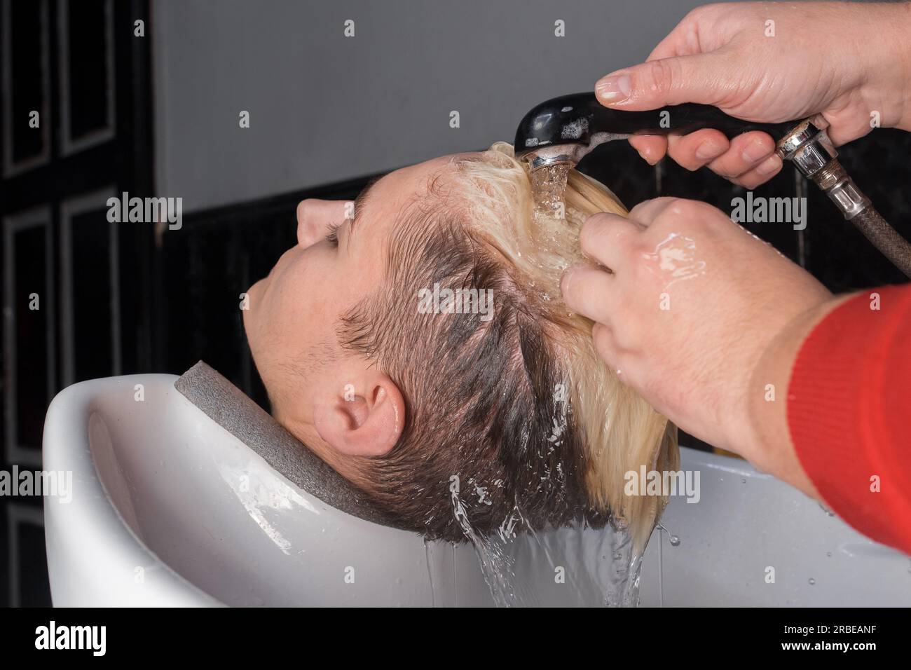 Nahaufnahme, wie du dir die Haare mit Regen über der Spüle eines Klienten wäschst, bevor du in einem Friseursalon die Haare schneidest. Stockfoto