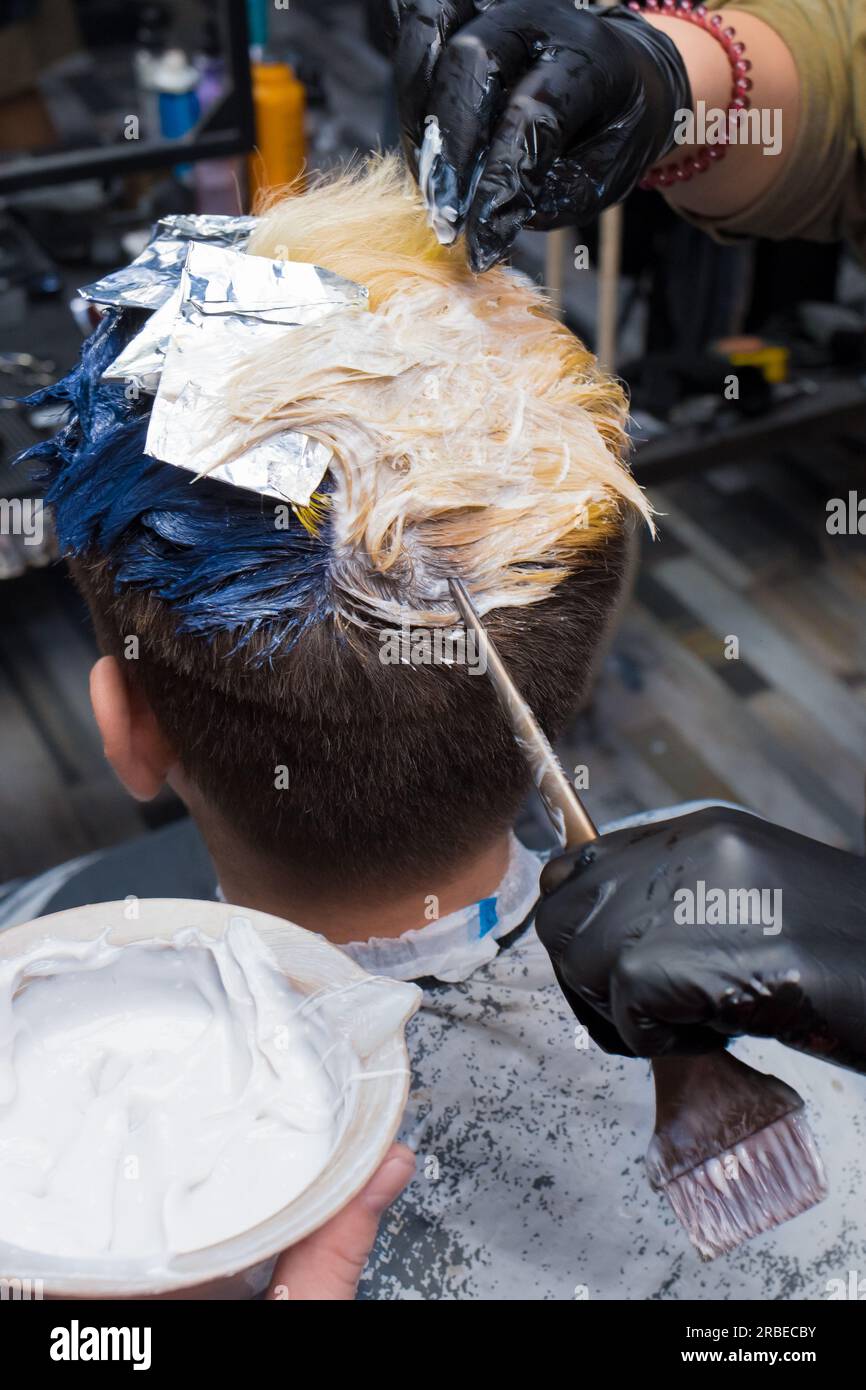 Die Hände eines professionellen Friseurs halten in einem Friseursalon bei der Arbeit eine Bürste zum Färben von Männerhaaren neben weißem Farbstoff. Stockfoto