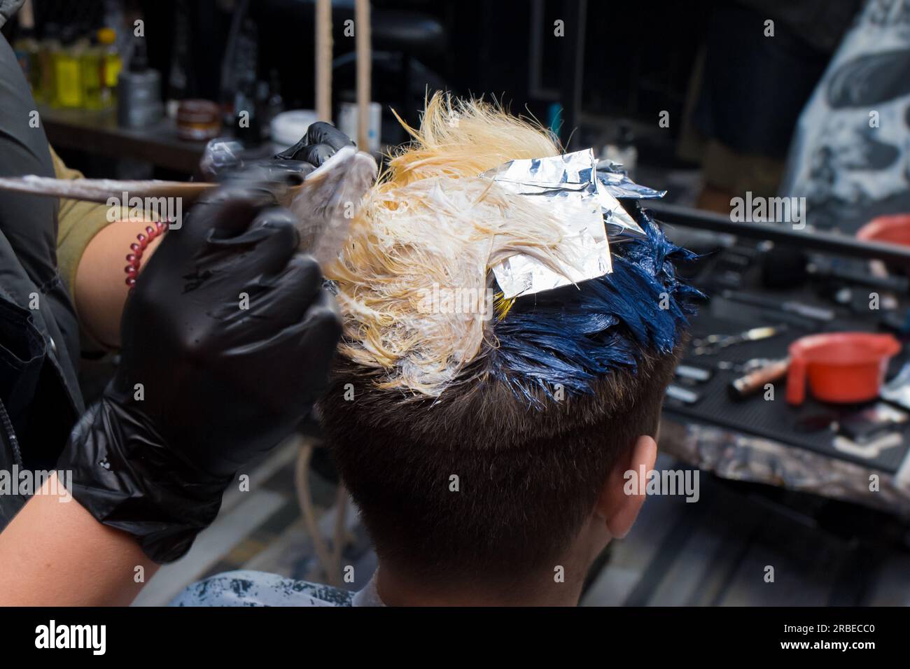 Nahaufnahme der farbigen männlichen Haarfärbung mit einer Bürste durch einen professionellen Friseur bei der Arbeit. Stockfoto